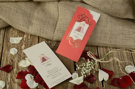 A Red And White Wedding Card On Top Of A Wooden Table Next To Some Flowers