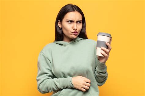 Joven latina encogiéndose de hombros sintiéndose confundida e insegura dudando con los brazos