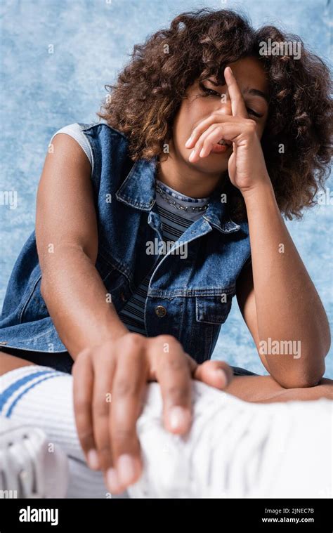 Brunette African American Woman In Denim Vest Obscuring Face With Hand