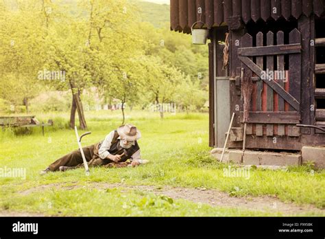 Old Farmer With Beard Is Repairing His Scythe Before Using To Mow The