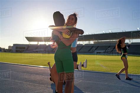 Happy Female Track And Field Athletes Hugging On Sunny Track Stock