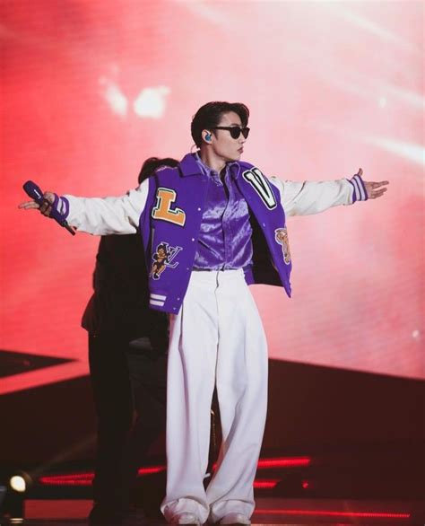 A Male In A Purple Jacket And White Pants Is On Stage With His Arms Out