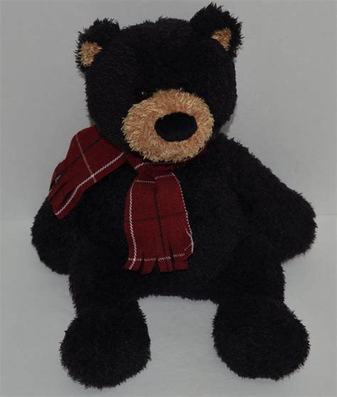 A Black Teddy Bear With A Red Scarf Around Its Neck Sitting On A White