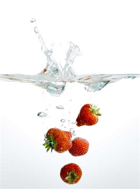 Fresh Strawberries Falling Into Water Against White Background Stock Photo