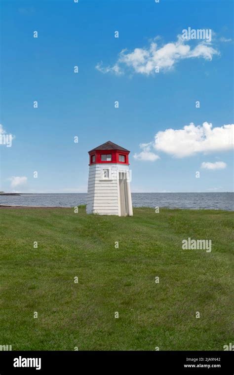 Small White And Red Roof Lighthouse By The Ocean On Green Grass With