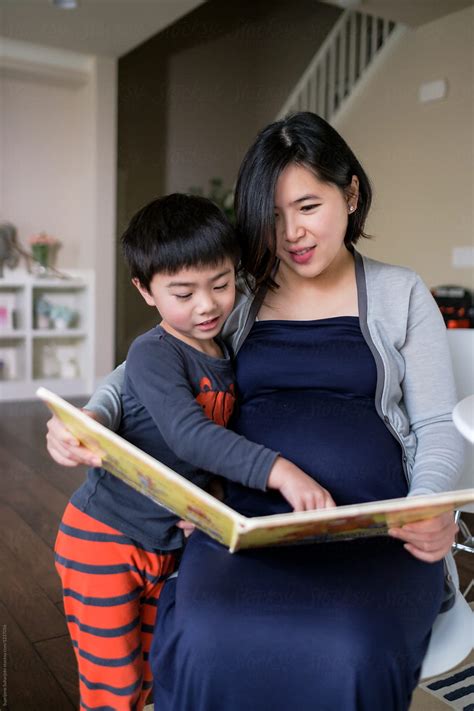 Pregnant Asian Woman Reading A Book With Her Son At Home By Stocksy