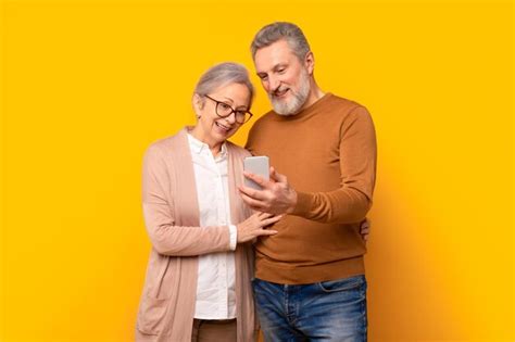 Premium Photo Happy Mature Gray Couple Looking At Smartphone Screen Hugging Studio