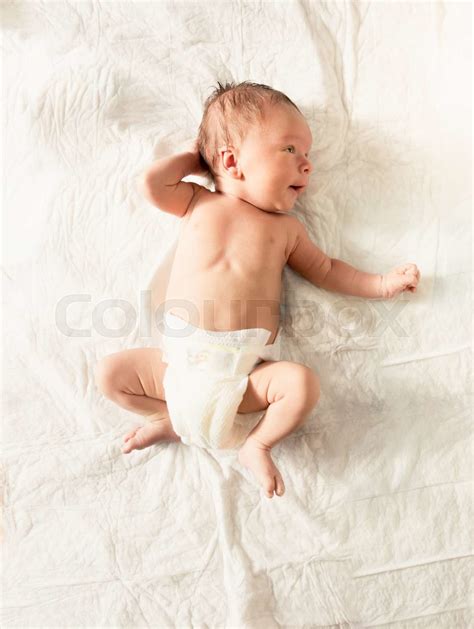 Cute newborn baby in diapers lying on white sheets on bed | Stock image ...