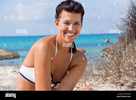 Schöne junge Frau mit einem schönen warmen Lächeln in einem Bikini am Strand auf einer Sanddüne