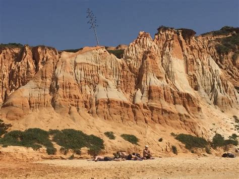 Some People Are Sitting On The Sand Near A Large Rock Formation With