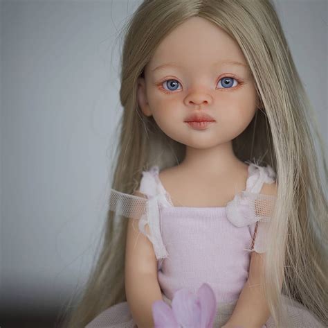 A Doll With Long Blonde Hair Wearing A Pink Dress And Holding A Purple