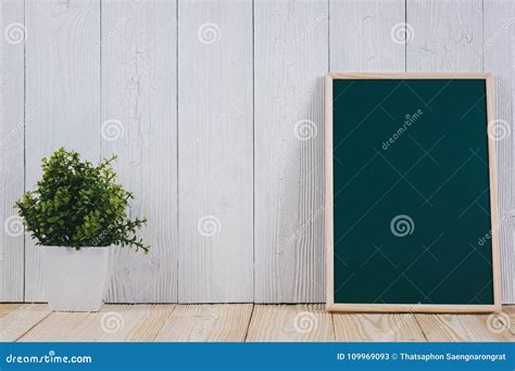 Blank Green Chalkborad With Wood Frame And Little Decorative Tree In White Vase On Wooden Table