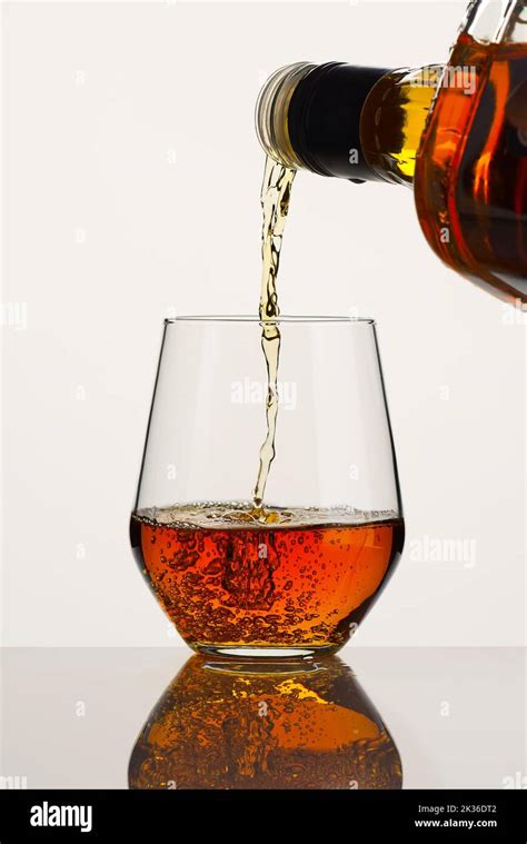 Whiskey Or Brandy Being Poured Into A Glass From Bottle On White