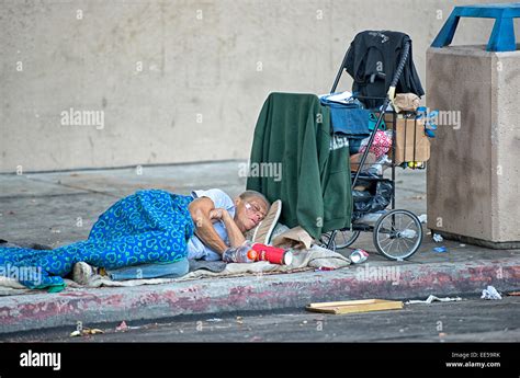 Homeless Elderly Woman Sleeping On Sidewalk Next To Shopping Cart And