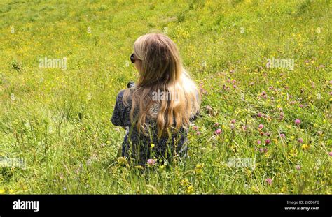 A Pretty Blonde Woman Is Sitting On A Flower Meadow Stock Photo Alamy