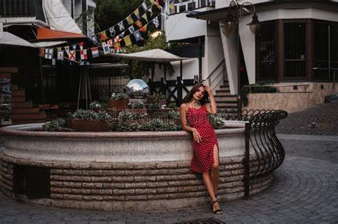 Beautiful Brunette Girl In A Red Dress Posing On Street With Paving
