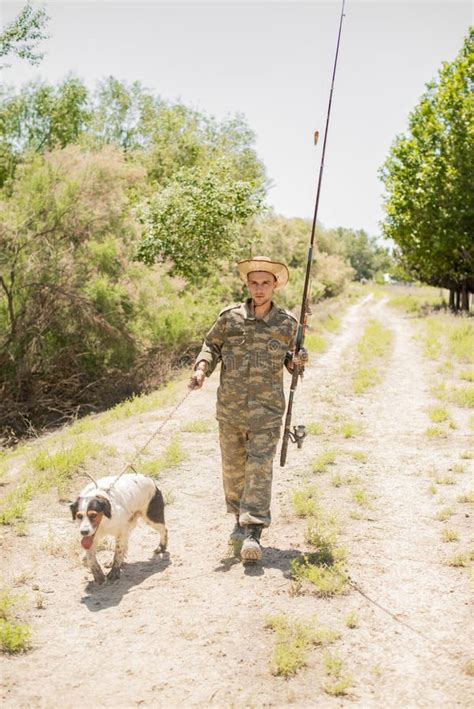 Focused Fisherman In Straw Hat And Camo Clothes Going Fishing With Dog