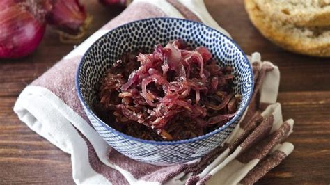 a bowl filled with red cabbage on top of a table next to bread and onions