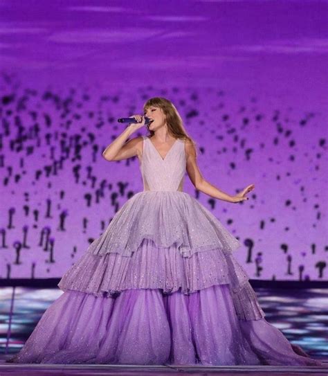 The Singer Is Wearing A Purple Gown And Holding A Microphone In Her