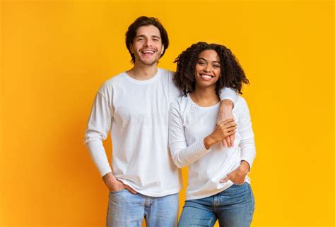 Happy Interracial Couple Cuddling While Posing Over Yellow Background