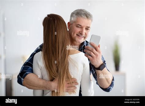 Mature Man Embracing His Wife Stuck In Smartphone Not Paying Attention Texting His Lover