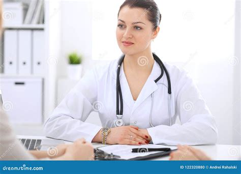 Brunette Female Doctor Talking To Patient At Hospital Office Physician Says About Medical Exams