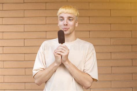 Satisfied Caucasian Guy Holding An Ice Cream Stick In His Hand Near His Face Looking At It With