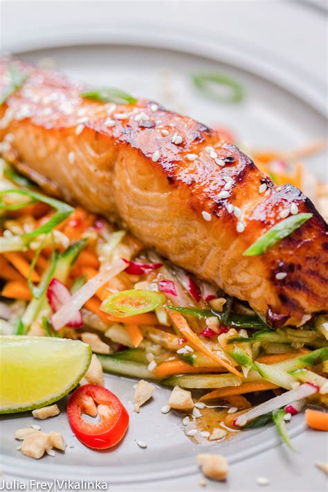 A White Plate Topped With Fish And Veggies Next To A Slice Of Lime