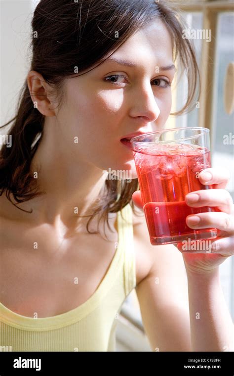 Female Brunette Hair Tied At The Back Wearing A Yellow Vest Standing By The Window Drinking