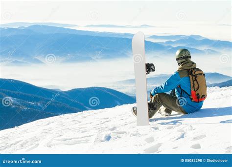 Male Snowboarder In Helmet Sitting At The Very Top Of A Mountain And