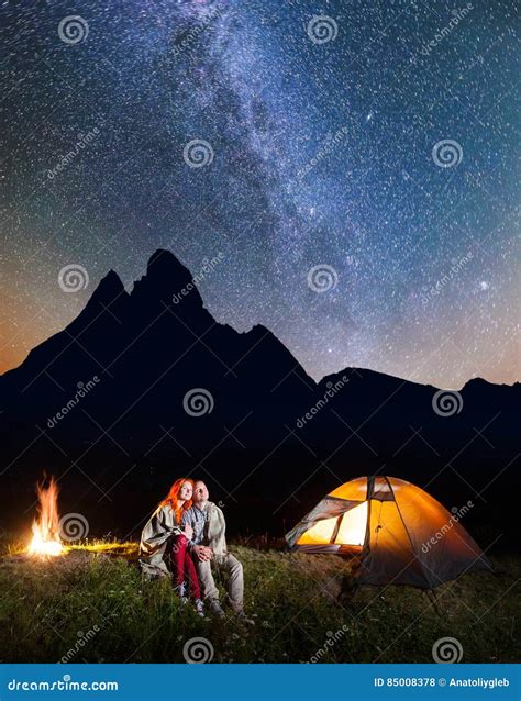 Couple Hikers Sitting Together Near Campfire and Glowing Tent at Night