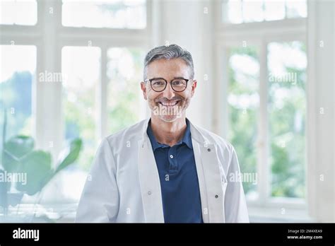 Happy Mature Doctor Wearing Eyeglasses Standing In Medical Practice