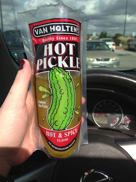 A Person Holding Up A Hot Pickle In Their Hand On The Dashboard Of A Car