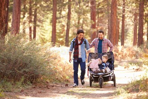 Pareja Masculina Gay Que Empuja a Niños En Cochecillo a Través Del Bosque Foto de archivo