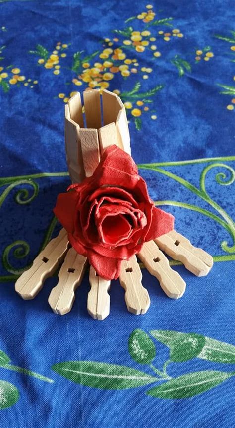 A Red Rose Sitting On Top Of Clothes Pins In Front Of A Blue Table Cloth