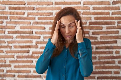 Brunette Woman Standing Over Bricks Wall With Hand On Head For Pain In Head Because Stress Stock