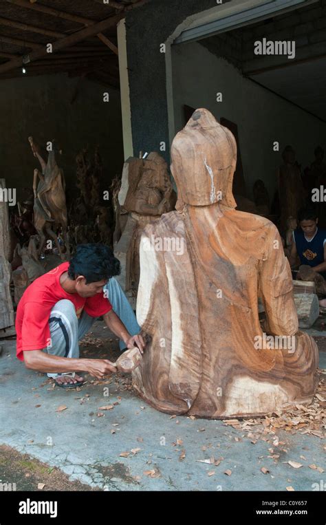 A Balinese Craftsman Wood Carver At Work On A Carving Of A Large Seated