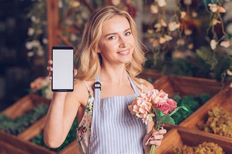 Souriant portrait d une jeune femme blonde tenant un bouquet à la main montrant un téléphone