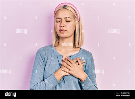 Beautiful Blonde Woman Standing Over Pink Background Smiling With Hands On Chest With Closed