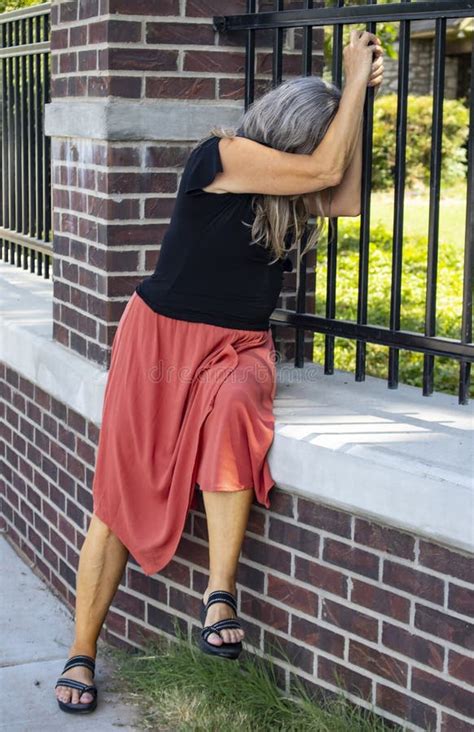 Gray Haired Woman In Trouble Wearing Dress And Sitting By A Fence At
