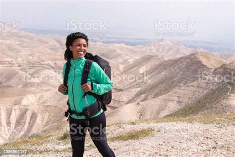 Happy African Woman Hiking Outdoors In Desert With Bag Stock Photo