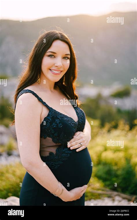 Pregnant Woman Hugging Her Tummy Is Standing On The Top Of A Rocky