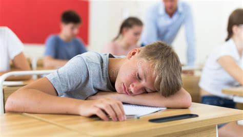 Bored Teenage Boy Sleeping At Desk In Classroom During Lesson Stock