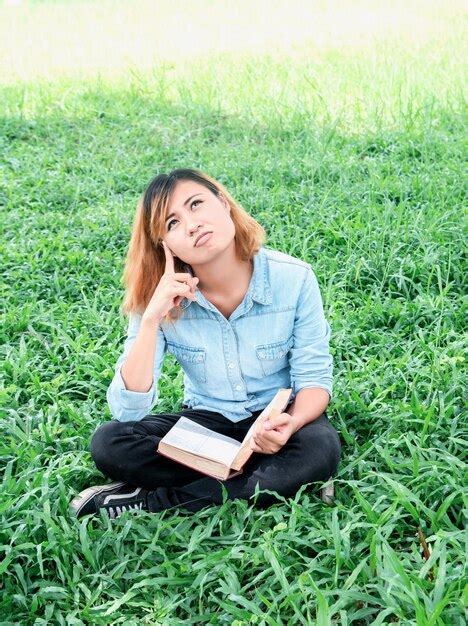 Premium Photo Thoughtful Woman Reading Book While Sitting On Field