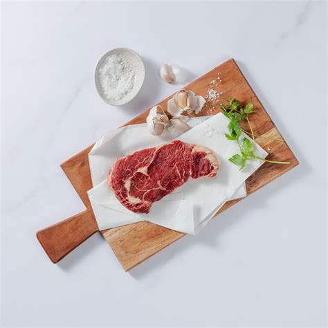 Silver Fern Farms Beef Rib Eye Steak Placed On Board With Garlic Cloves