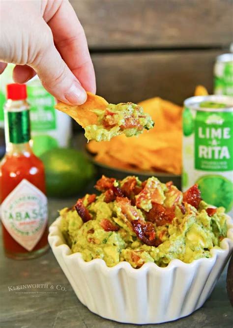 A Hand Holding A Tortilla Chip Over A Bowl Of Guacamole