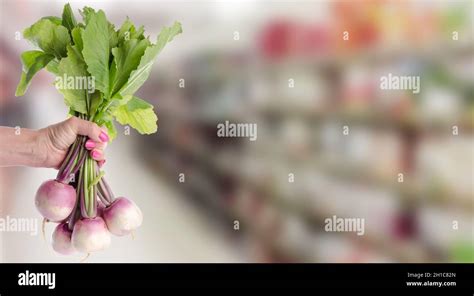 Hand Holding A Bunch Of Fresh Turnips With Blurred Supermarket Shelf On