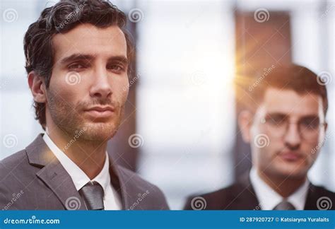 Two Serious Young Businessmen Standing With Arms Crossed In Office