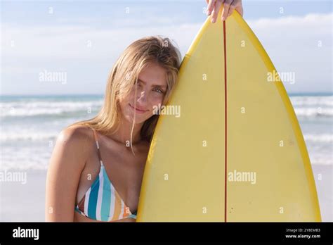 Caucasian Woman Wearing Bikini Carrying Surfboard Looking At Camera And