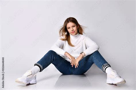 Teenage Female In Jeans Sweater Socks And Sneakers Smiling Sitting On Floor Legs Wide Apart